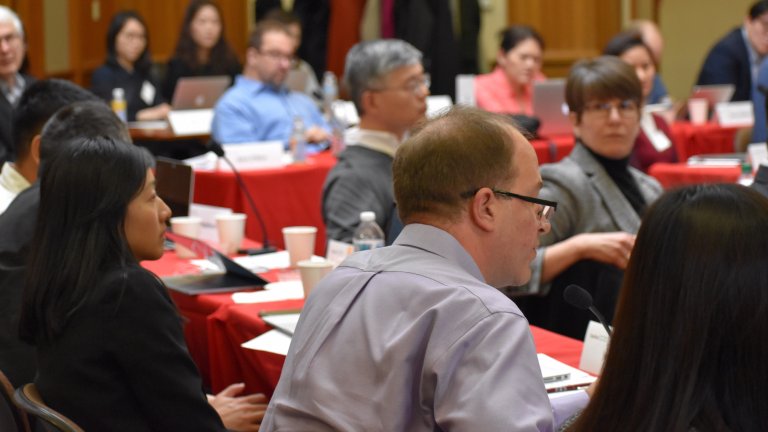 A group of people seated in a conference room listening to a man speaking