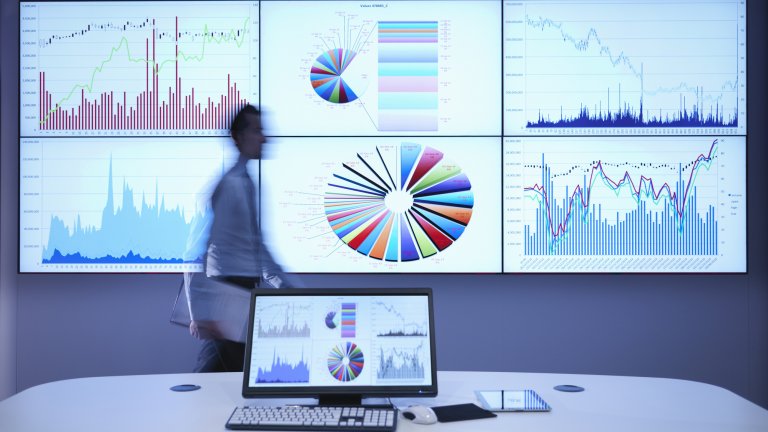 Businessman walking in front of statistical graphs on a screen.