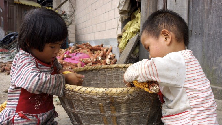 Young children sort corn outside of a home in a rural village in China.
