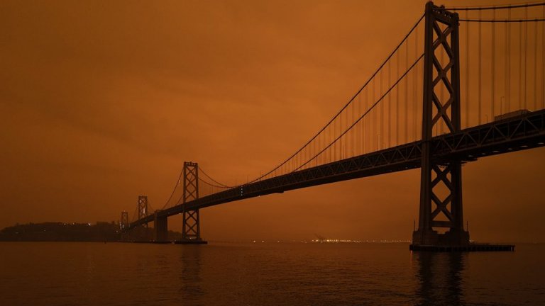 An orange smokey sky behind a dark bridge over water