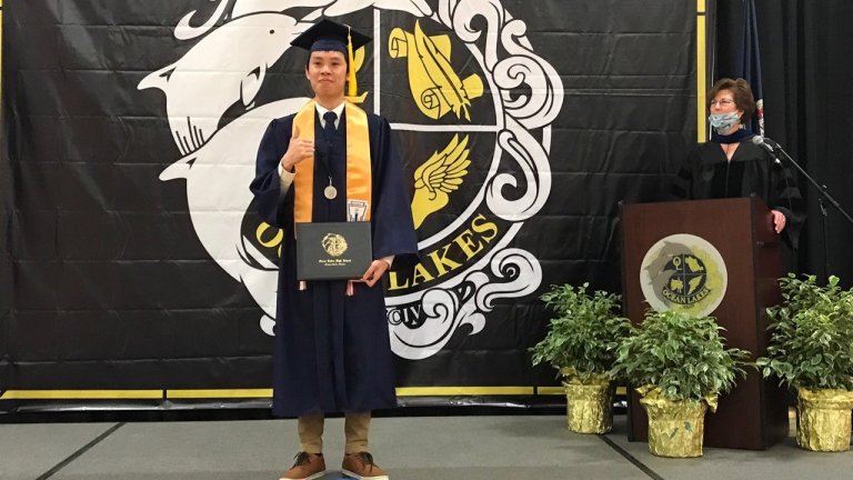 High school student with a diploma standing in front of a banner