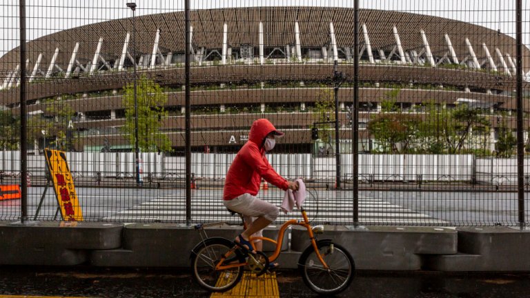 A man cycles past a security fence outside the New National Stadium, the main stadium for the Tokyo Olympics, on June 23, 2021 in Tokyo, Japan