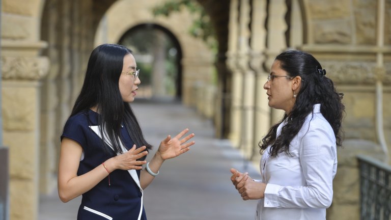 2018-19 postdoctoral scholars Ketian Zhang and Sarita Panday in conversation at the Encina Hall entranceway.