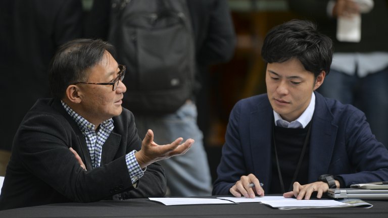 Two men seated in discussion over a paper on the table