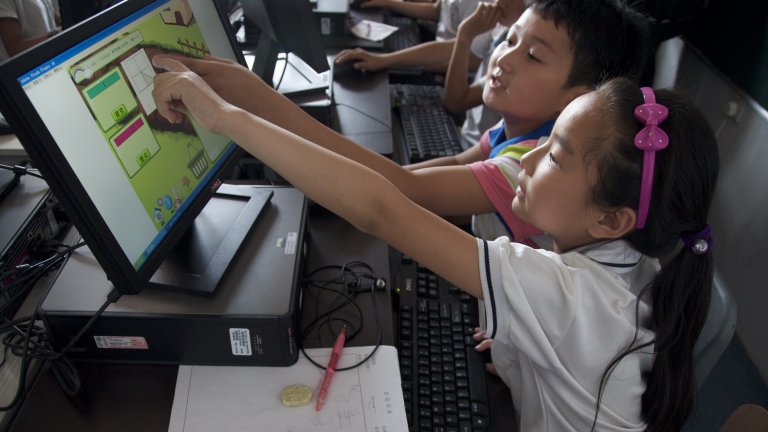 Two students sitting in front of a computer screen and pointing to a the computer screen that has a game on it.