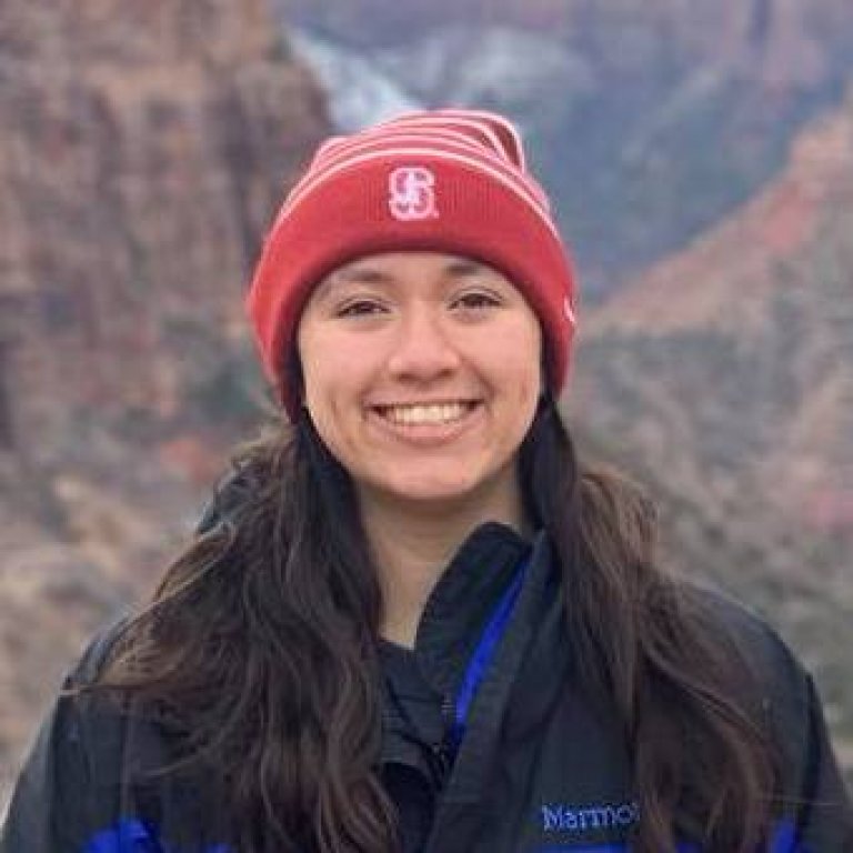 A headshot of Isabella Khuu. Isabella is wearing a red stanford hat and standing at the edge of the grand canyon.