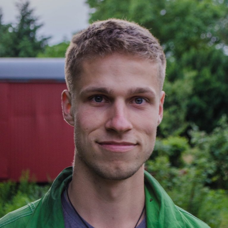 A headshot of Justin Braun. Justin is smiling slightly and standing outside.