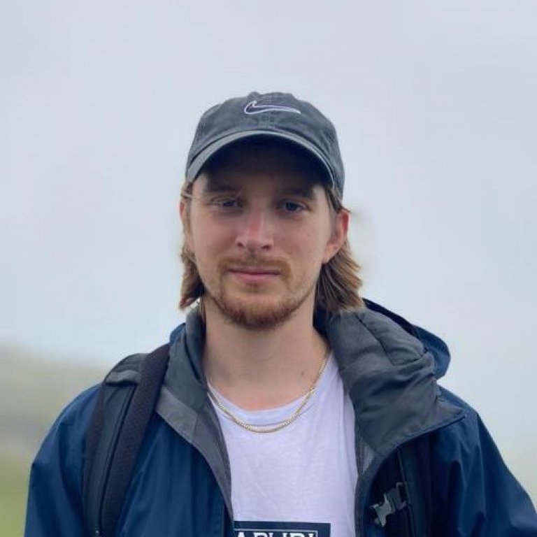 A headshot of Chris Giles. Chris is smiling slightly with the Scottish countryside behind him.