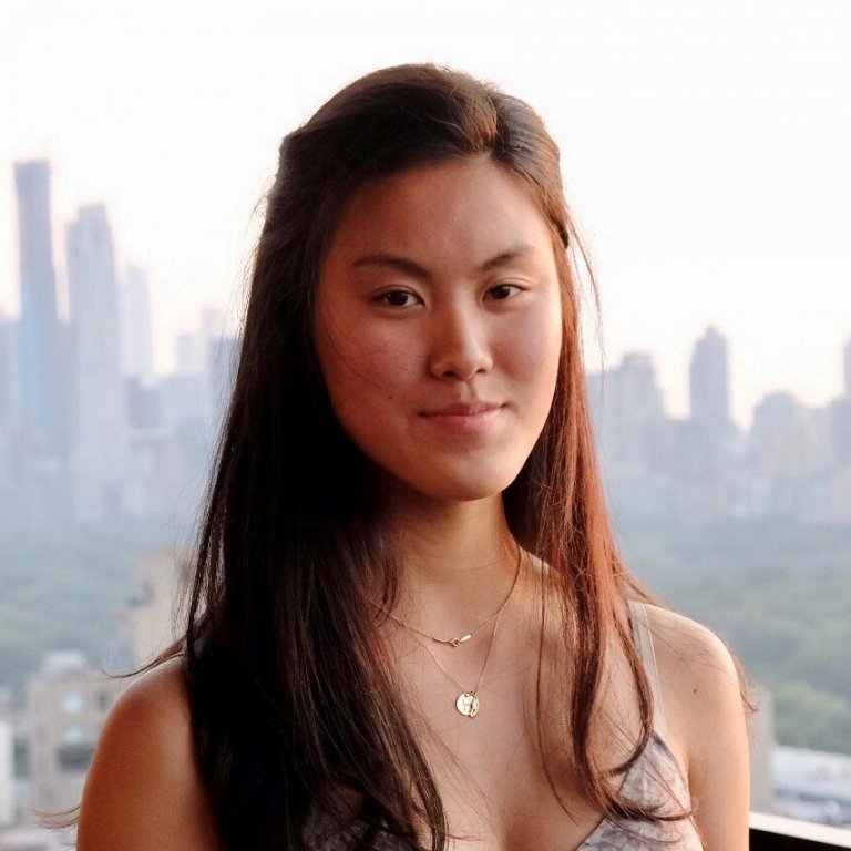 A headshot of Hanna Yip. Hanna is standing on a rooftop and has a faded skyline behind her.