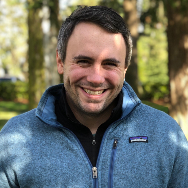 Headshot of Austin Buscher. Austin is smiling and wearing a blue coat.