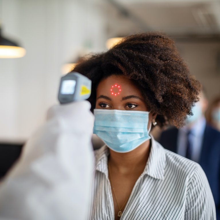 A Black woman wearing a mask gets her temperature taken.