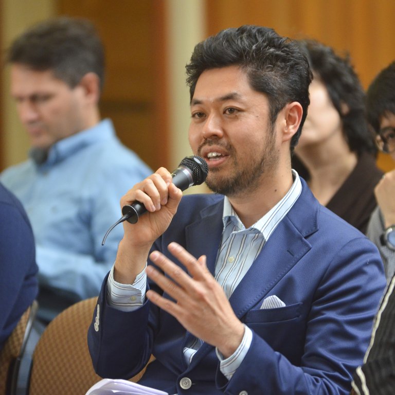 Global Affiliate Visiting Fellow speaks to a microphone while seated among an audience at an APARC event.