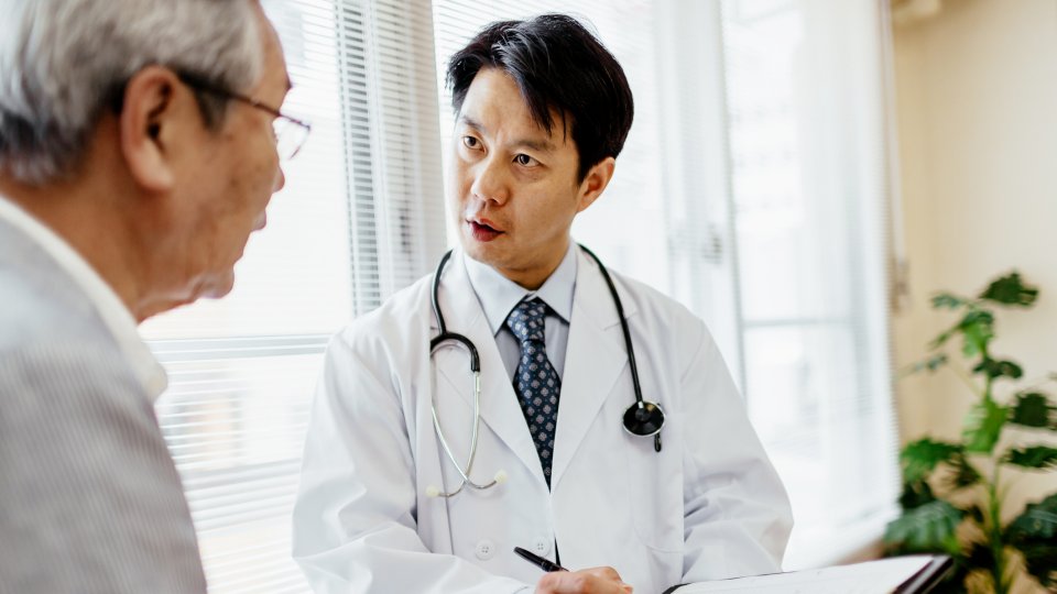 Male Japanese doctor showing senior patient records on a clipboard