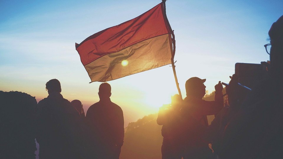 Silhouettes carrying a flag of Indonesia with a sunset or sunrise in the background