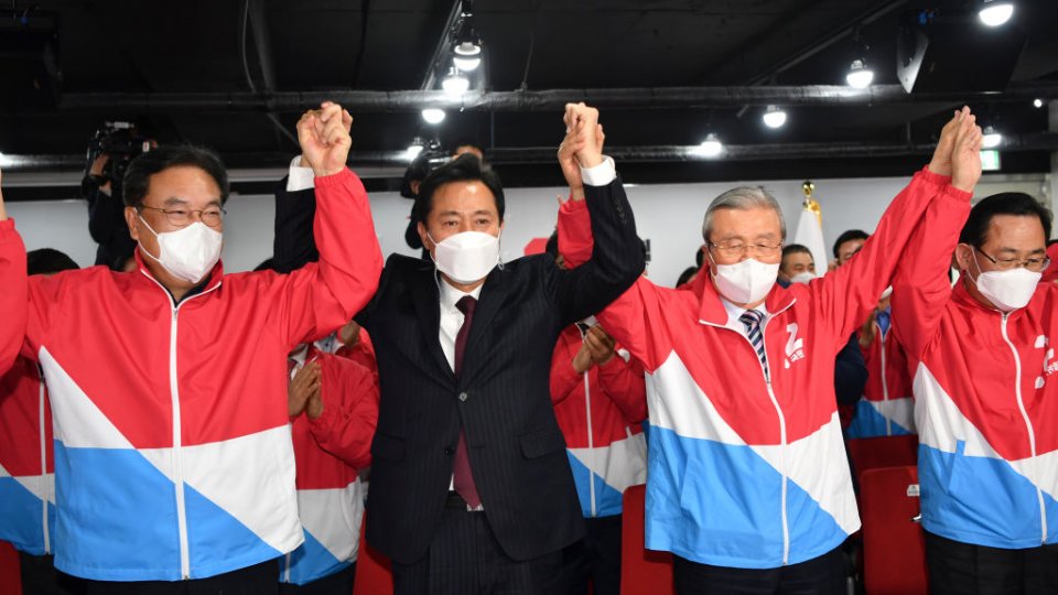 South Korean men standing up, wearing face masks, holding hands and cheering