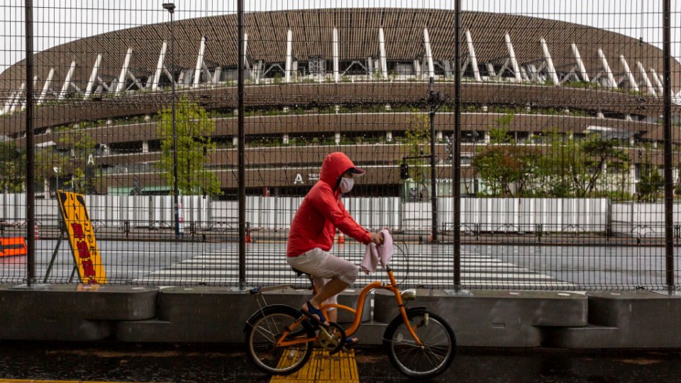 A man cycles past a security fence outside the New National Stadium, the main stadium for the Tokyo Olympics, on June 23, 2021 in Tokyo, Japan
