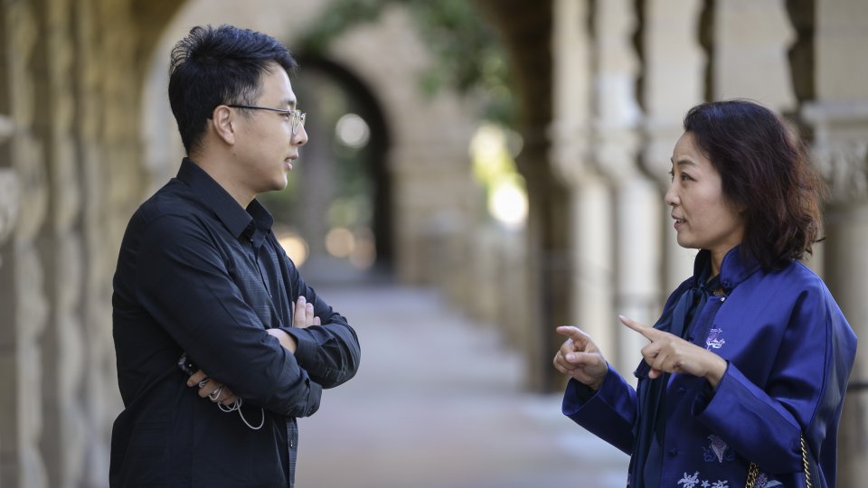 Two young scholars (man and woman) speaking at Encina Hall colonnade