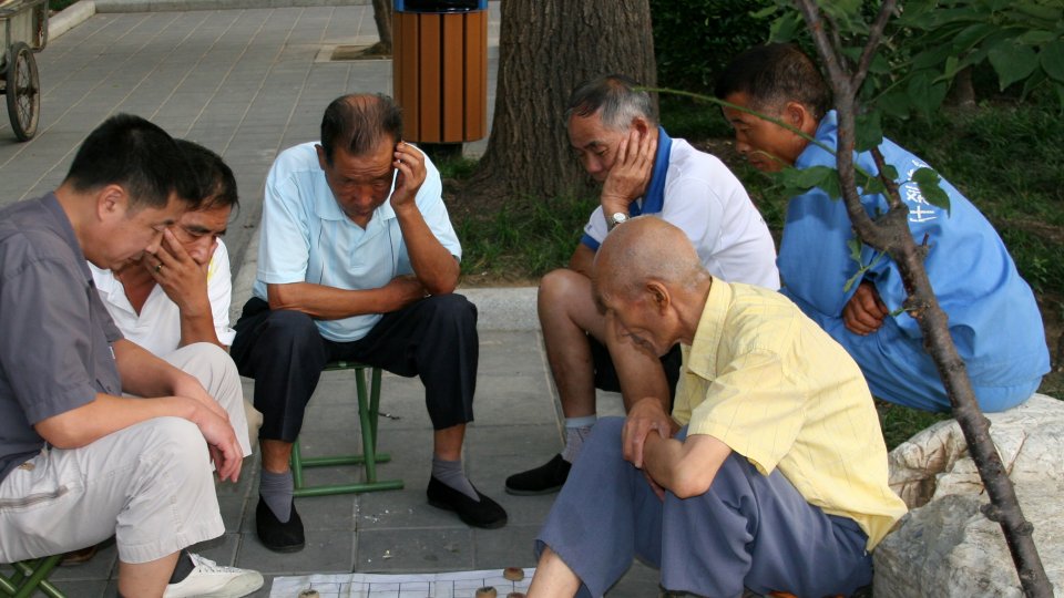 A group of Chinese elderly men sit outdoors, playing a game. A group of Chinese elderly men sitting outdoors, playing a board game.