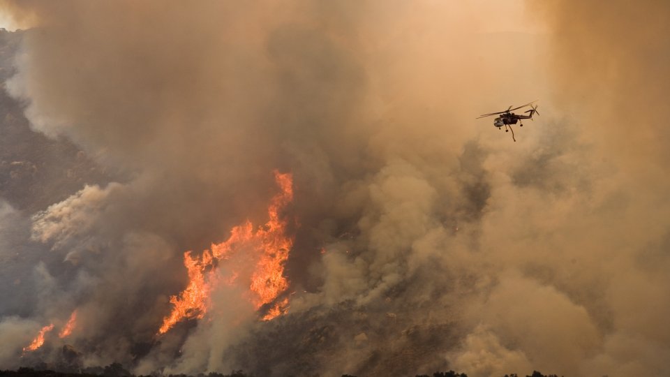 Helicopter flying over large brown plumes of smoke coming from a wildfire