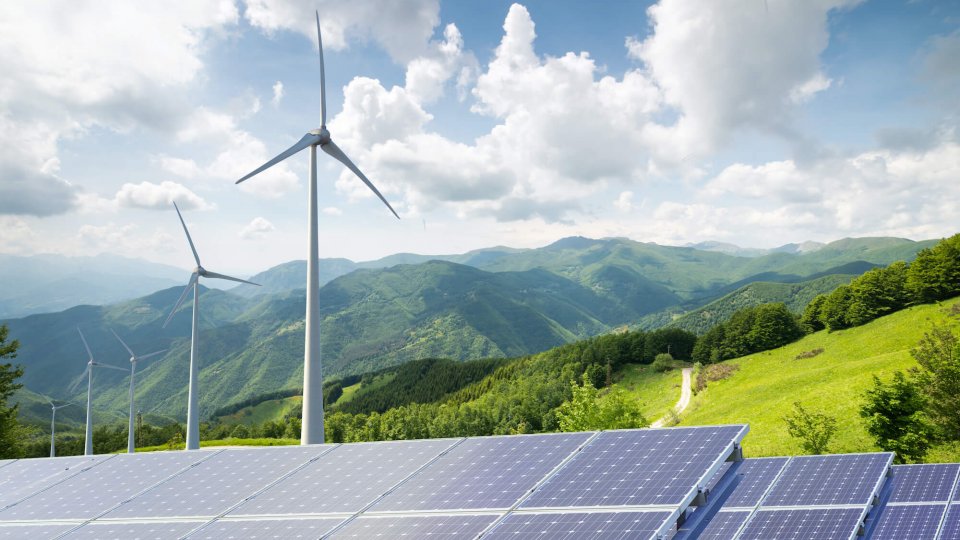solar panels with wind turbines against mountain landscape against blue sky with clouds