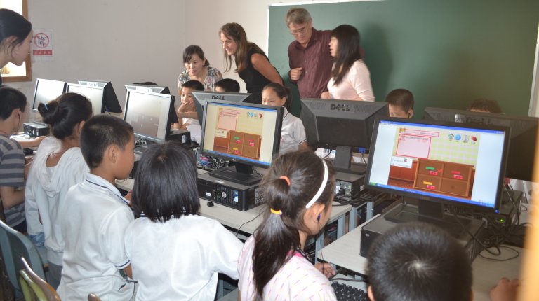 School kids sit in a row working on desktop computers.