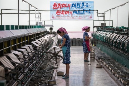 Women work a silk factory beneath a banner with Korean writing.