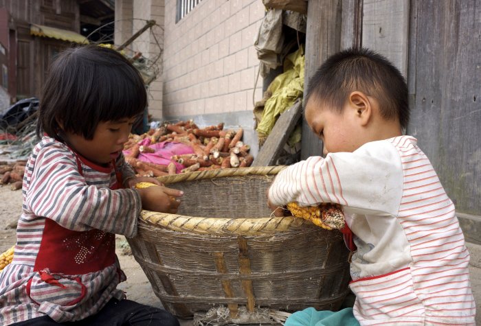 Young children sort corn outside of a home in a rural village in China.