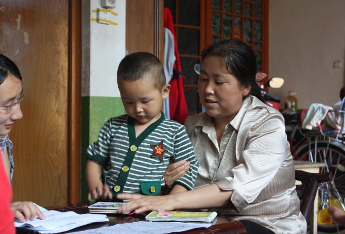 A toddler and his caregiver looking at a book together at a table in a home.