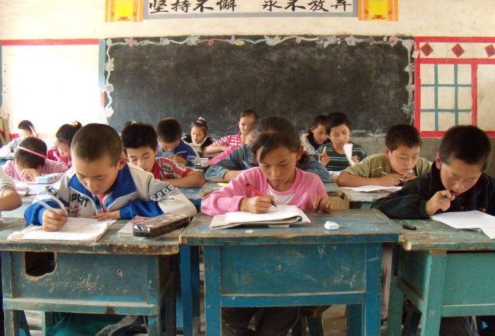 Middle school kids work at desks in a run down classroom in rural China.