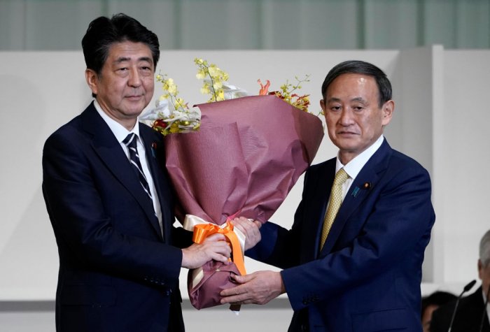 Japan's outing Prime Minister Shinzo Abe and incoming Prime Minister Yoshihide Suga hold a flower bouquet