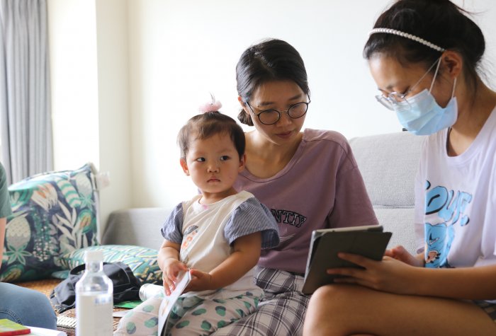 Migrant child sits on her mother’s lap, looking into the camera, as her mother reviews REAP’s survey forms with an enumerator.