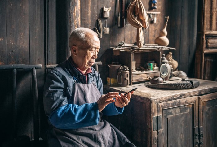 Chinese senior man tapping on mobile phone in wooden house.