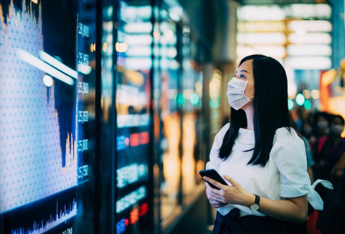 Woman in a face mask looking at a stock market board