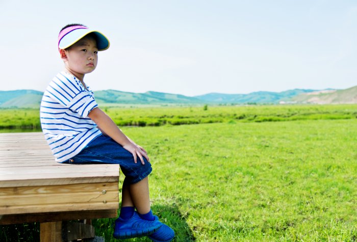 A boy sits alone on a wood deck over a green field in China.