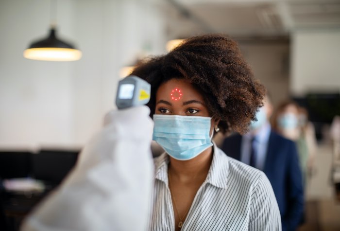 A Black woman wearing a mask gets her temperature taken.