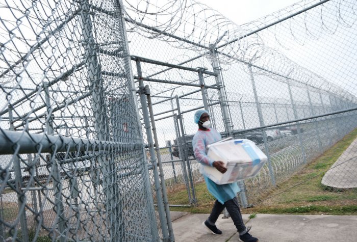 A health-care worker carries COVID-19 vaccines into a prison.