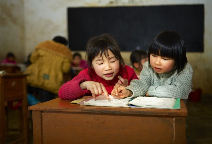 Chinese school children sit at a desk in a rural village school classroom.