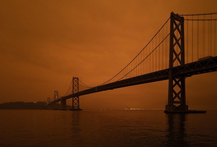 An orange smokey sky behind a dark bridge over water