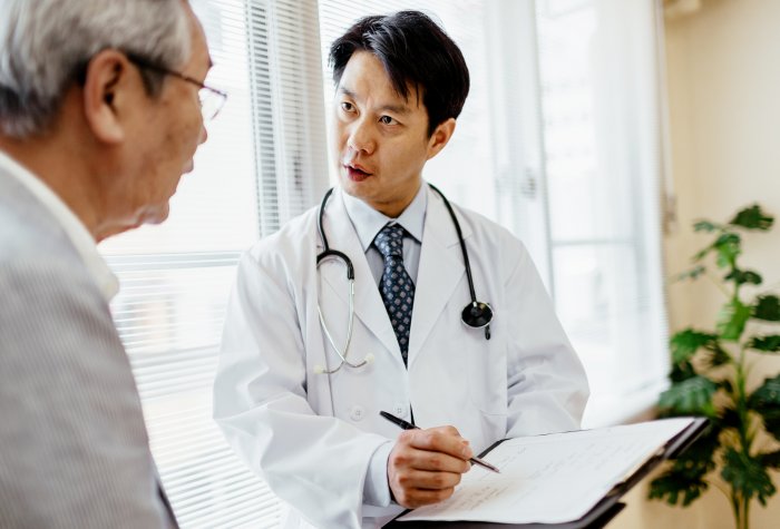 Male Japanese doctor showing senior patient records on a clipboard