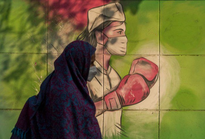 A woman walks past a mural referring to the Covid-19 coronavirus painted on a wall on December 10, 2020 in New Delhi, India.