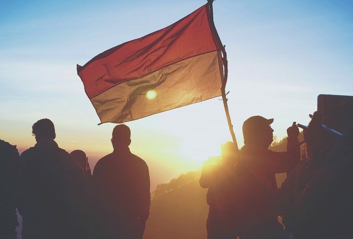 Silhouettes carrying a flag of Indonesia with a sunset or sunrise in the background