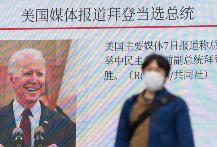 A man walks past a digital screen showing images of President-elect Joe Biden in a news program.