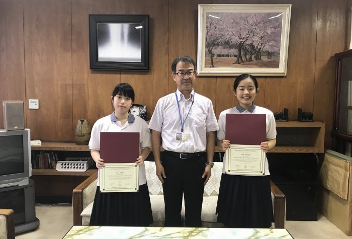 Two students holding diplomas with a principle in a room
