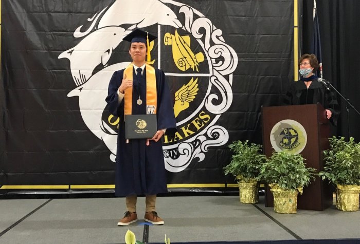 High school student with a diploma standing in front of a banner