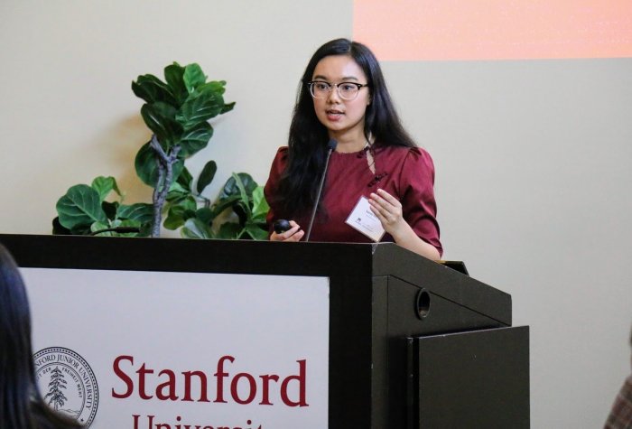 Student in a red dress presenting at a podium with Stanford signage