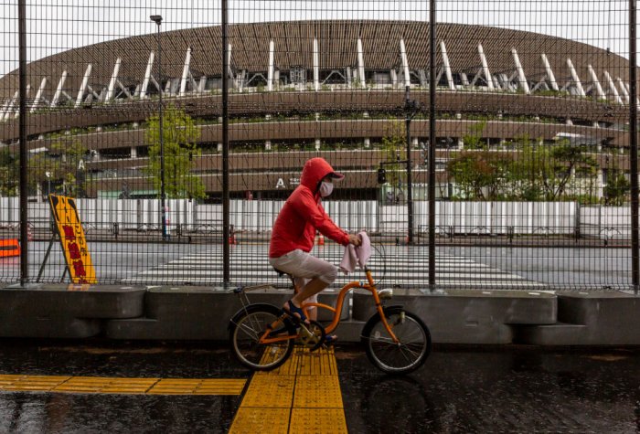 A man cycles past a security fence outside the New National Stadium, the main stadium for the Tokyo Olympics, on June 23, 2021 in Tokyo, Japan