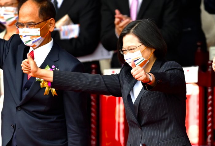 An Asian woman waring a face mask standing among a crowd gesturing with her hands