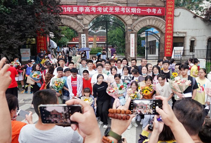 Crowd takes photos on their smartphones of a group of graduates in front of a Chinese university.