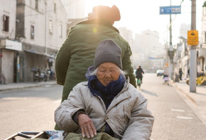 An elderly individual travels in a cart up a street.