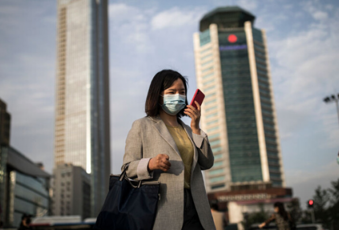 A professional looks at their phone while wearing a mask in a busy downtown area.